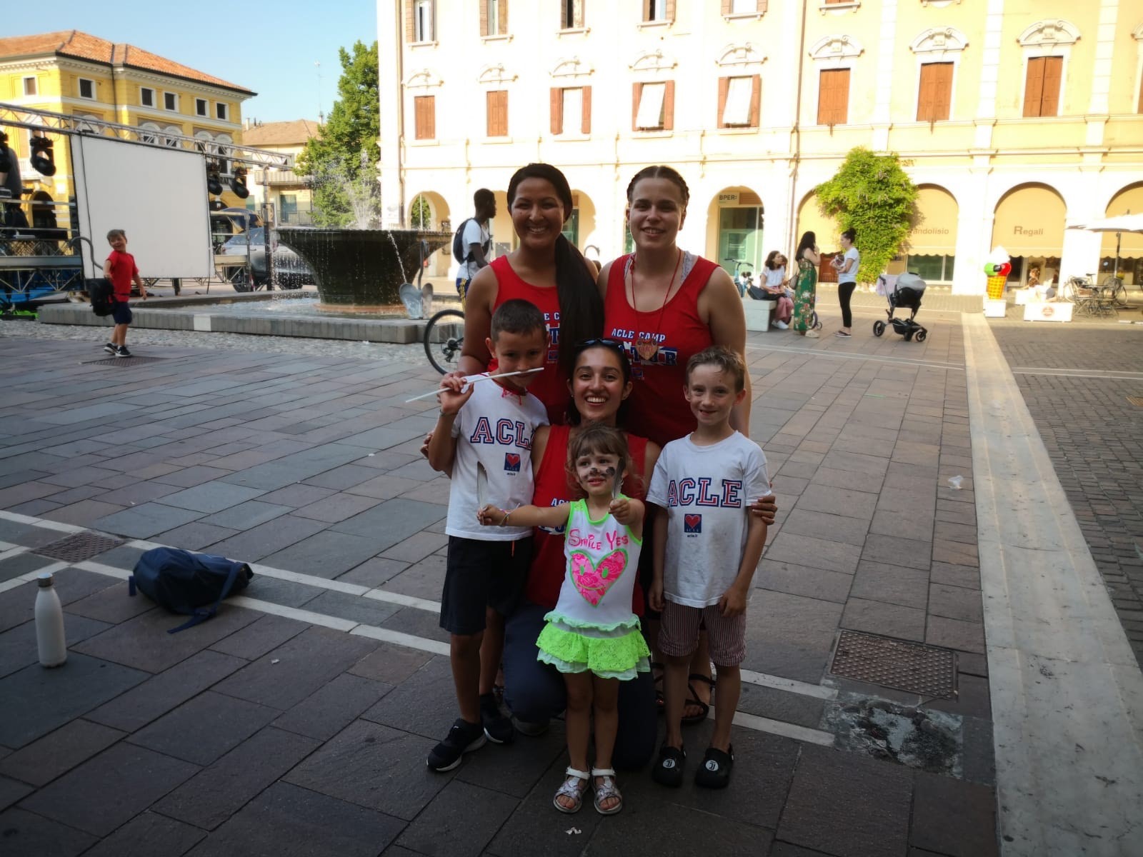 Three young women in red camp counselor uniforms pose with three young campers in Venice.